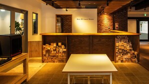 A reception area with a wooden counter, a white table, and stacks of wooden blocks. - Mori no Guest House - Hostel (Tenri)