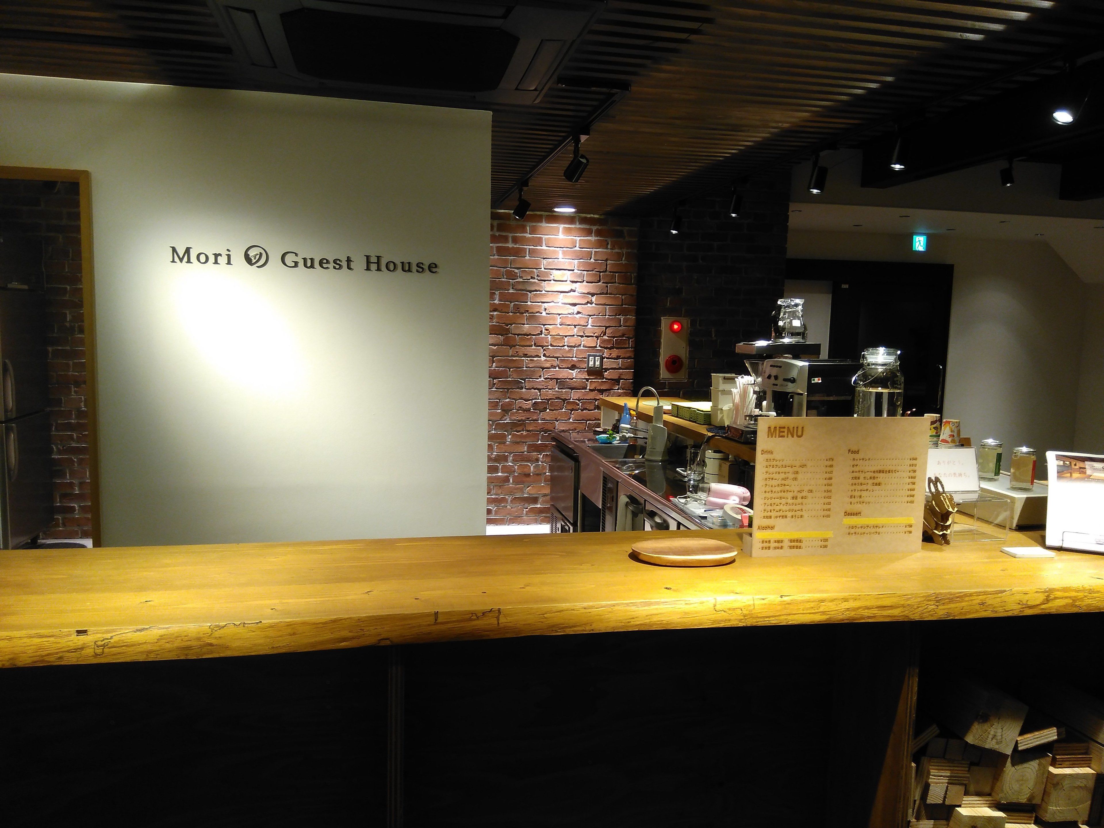A counter with a menu board, a brick wall, and a sign reading "Mori Guest House".