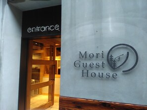 De ingang van een hotel genaamd 'Mori Guest House', met zichtbaar houten interieur door de glazen deur.