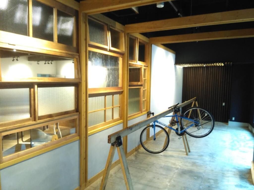A room with large wooden-framed windows, a bicycle, and a concrete floor.