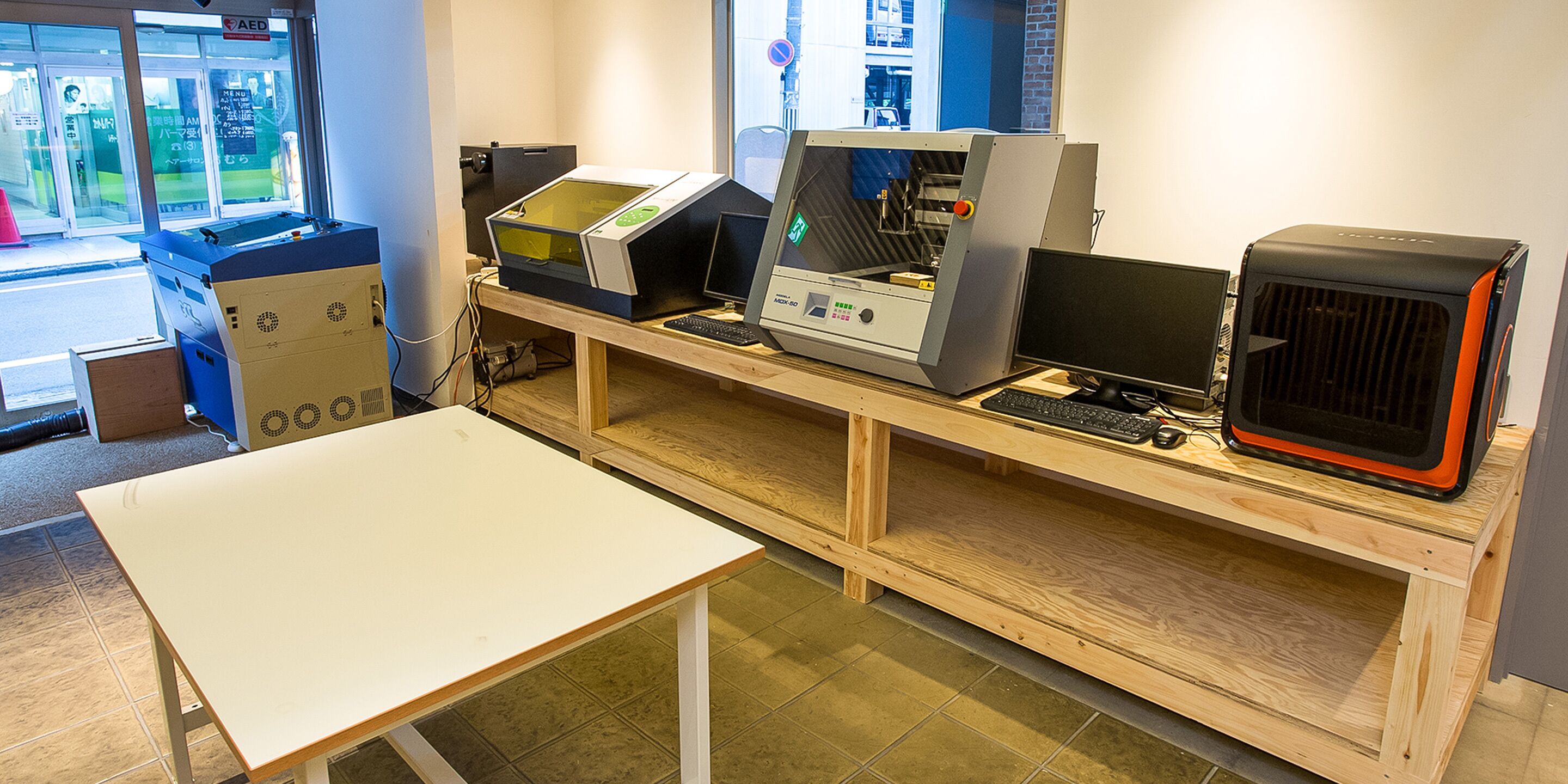 Ein Zimmer mit einem Holztisch, einem Computer und einer großen Maschine.