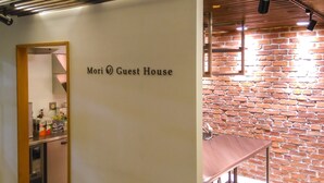 A sign reading "Mori Guest House" in a hallway with a brick wall and a wooden door frame. - Mori no Guest House - Hostel (Tenri)