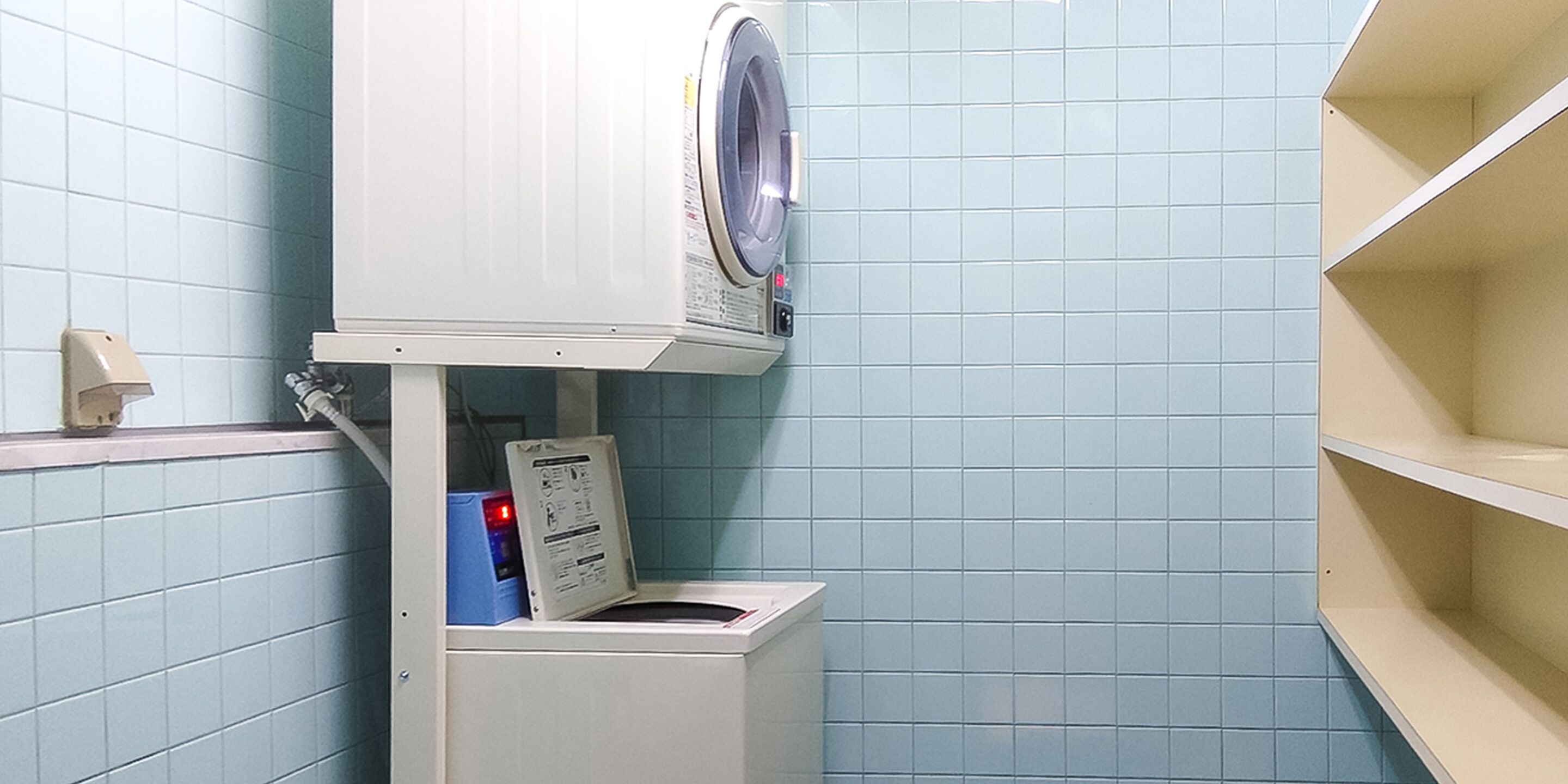 A compact, modern laundry room with a built-in washer and dryer, a control panel, and a blue-tiled wall.