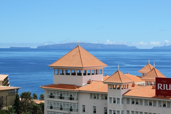 Un edificio costero con techo de tejas, vista al mar y una cadena montañosa distante.