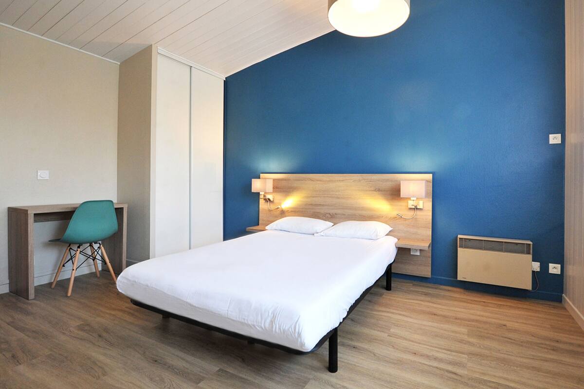 A modern hotel room with a large bed, a desk, and a chair.
