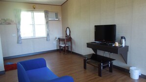 A room with a blue sofa, a wooden desk with a TV, a small table, and a window with curtains. - Dulan Red House (Donghe)