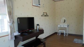 Una habitación con una televisión sobre un mueble de madera, un tocador blanco con espejo y una mesita con una tetera.