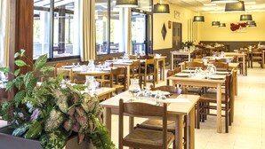Een restaurant met verschillende tafels en stoelen, grote ramen en hangende lampen.