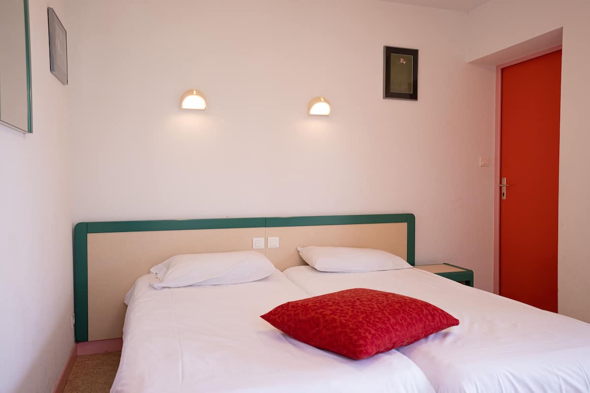 Une chambre d’hôtel avec un lit, deux tables de chevet et une porte rouge.