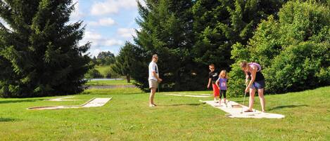 Un grupo de personas jugando croquet en un campo cubierto de césped, con árboles al fondo.