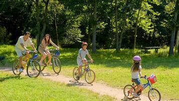 A family riding bicycles on a dirt path surrounded by trees.