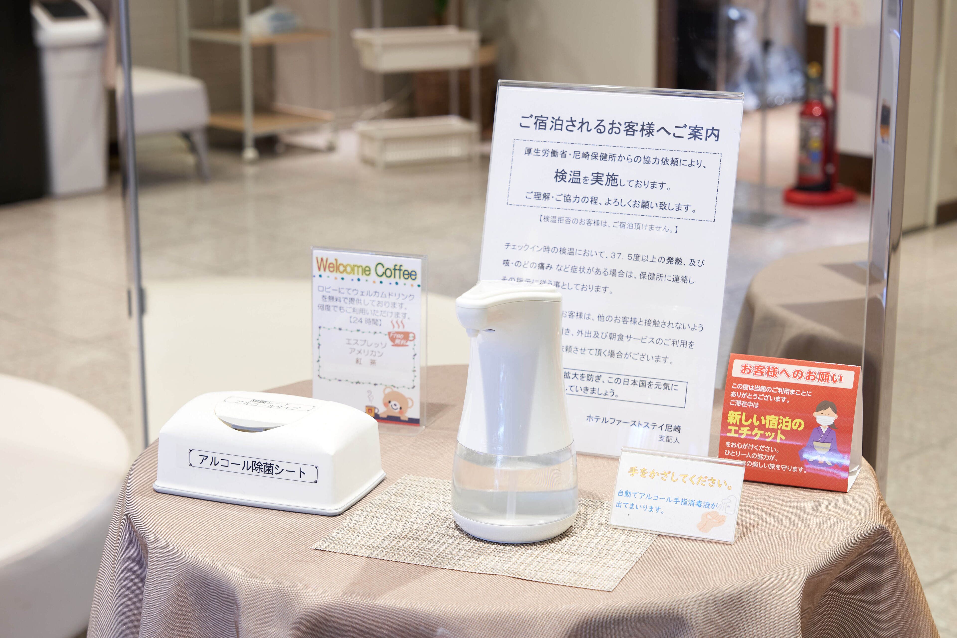 Una cafetera y un cartel con texto en japonés sobre una mesa en el vestíbulo de un hotel.