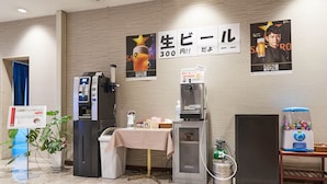 A hotel room with a minibar, a coffee machine, a small table with a tablecloth, a refrigerator, a water dispenser, and a vending machine. - Hotel First Stay Amagasaki (Amagasaki)
