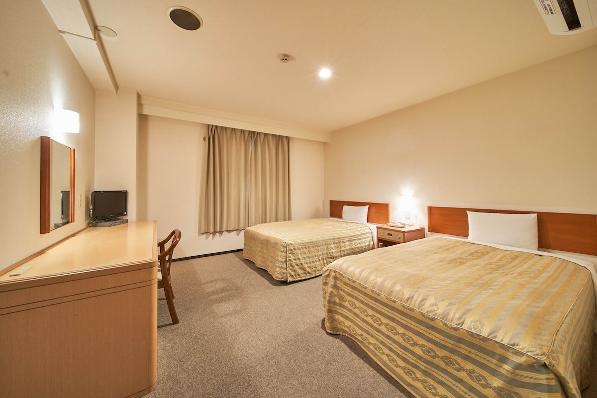 A hotel room with two beds, a desk, a chair, a television, and a window with curtains.