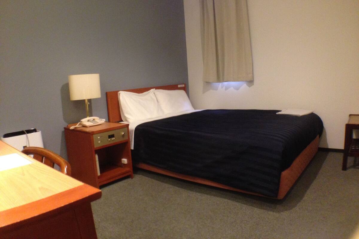 A hotel room with a bed, a desk, a lamp, and a telephone.