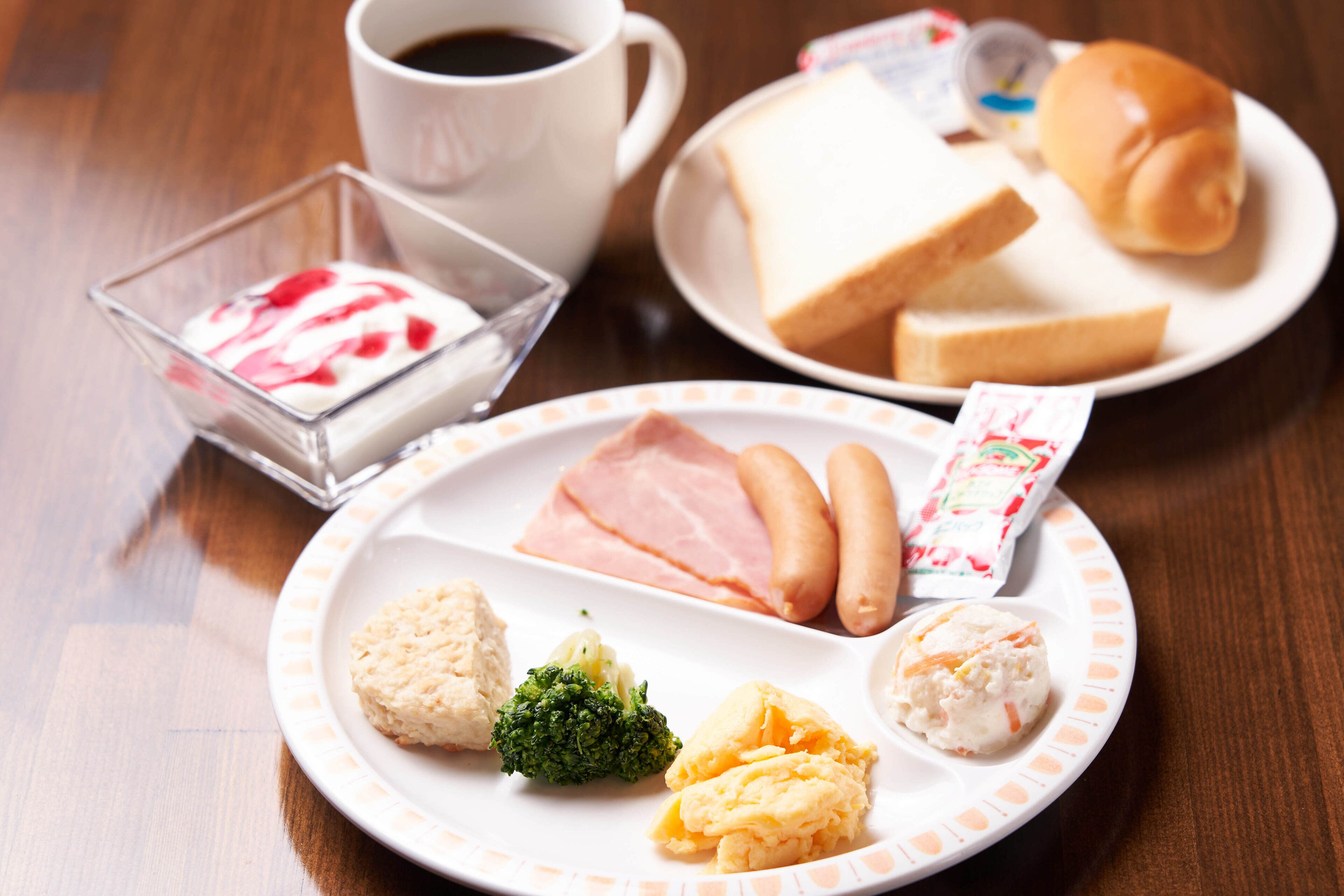 A meal with ham, sausages, biscuits, and a glass of milk on a table.
