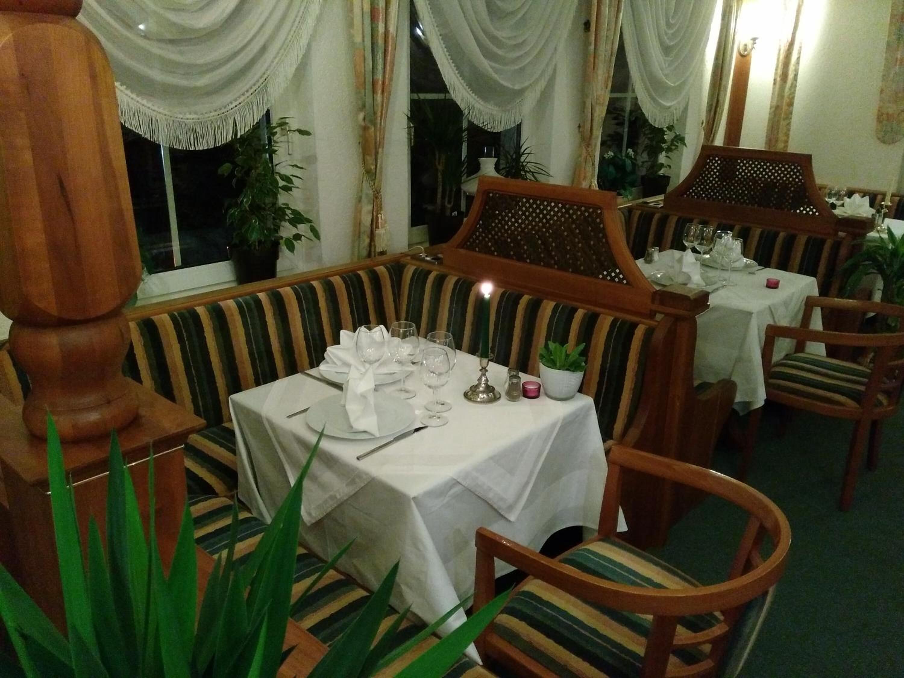 A dining area with striped upholstered booths, a table set for two with white tablecloths, and a candle centerpiece.
