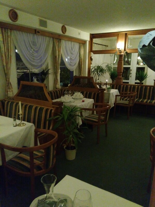 Un restaurante con mobiliario de madera, manteles blancos y plantas en macetas.