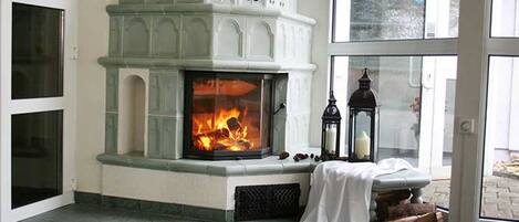 Una chimenea con fuego encendido, un banco cubierto con tela blanca y un farol.
