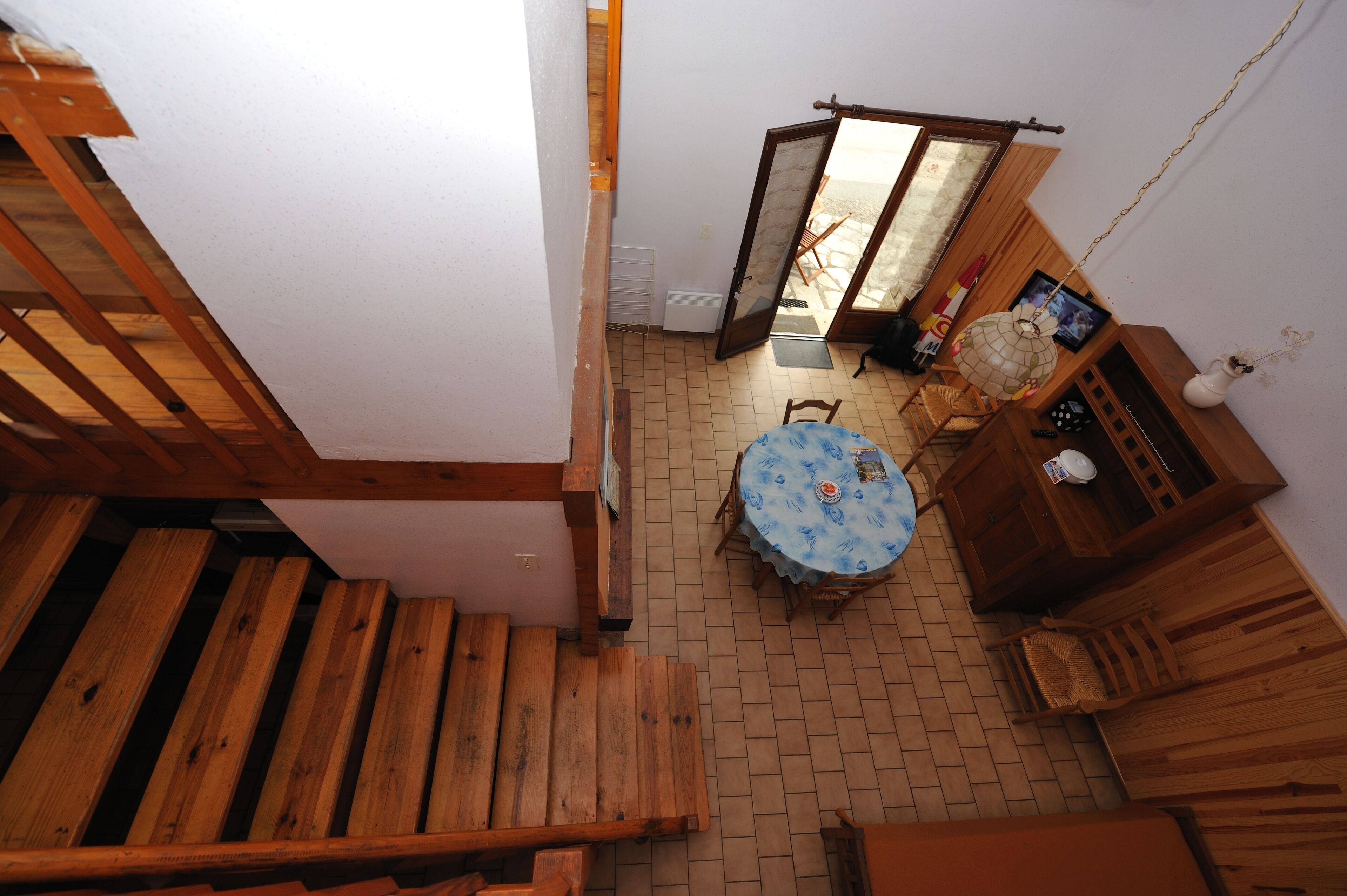 A compact room with a wooden staircase, a small round table with a blue tablecloth, and a wooden cabinet.