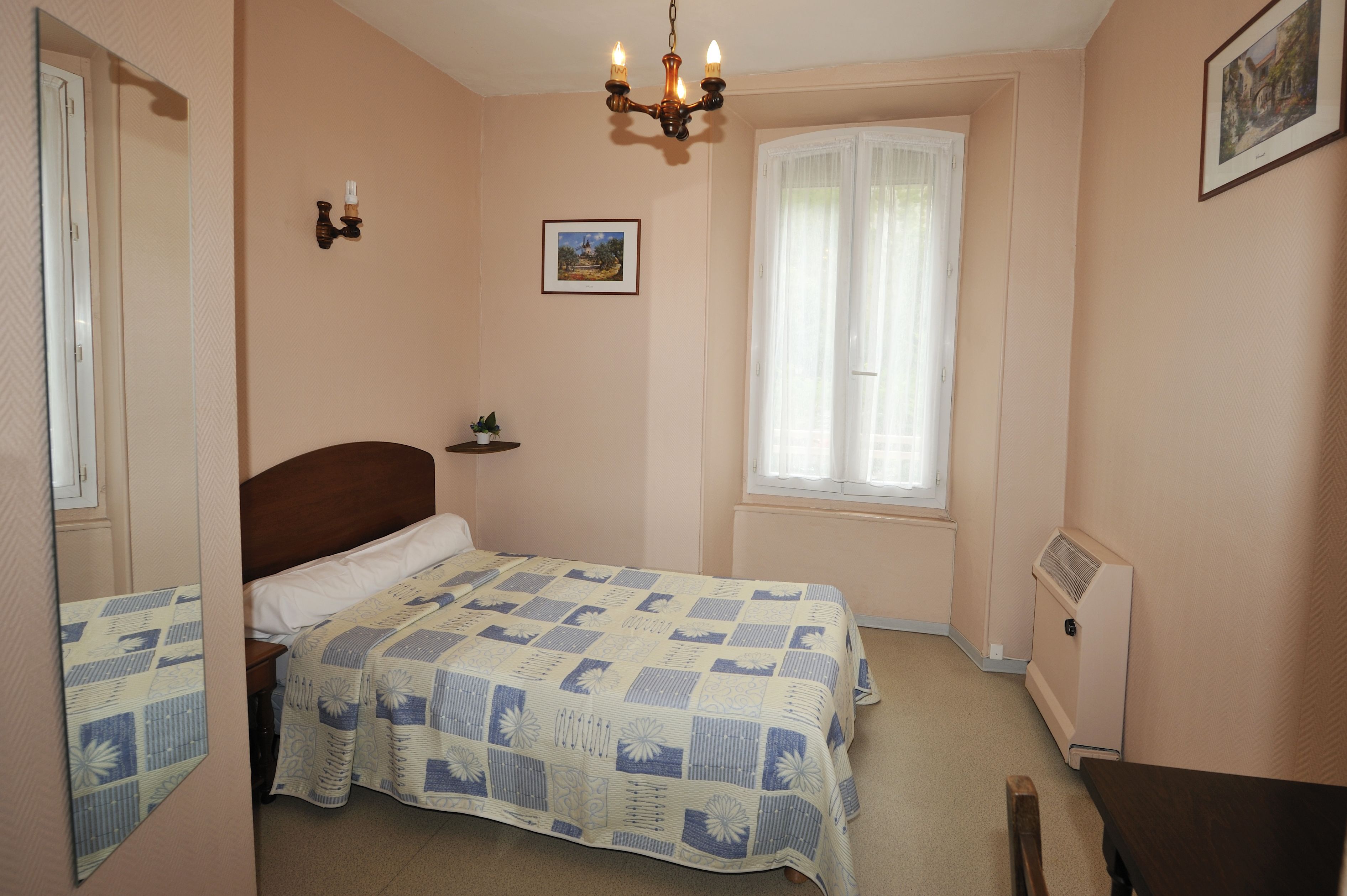 Ein Schlafzimmer mit Bett, Nachttisch, Vorhängen am Fenster, Heizkörper und einem Wandbild.