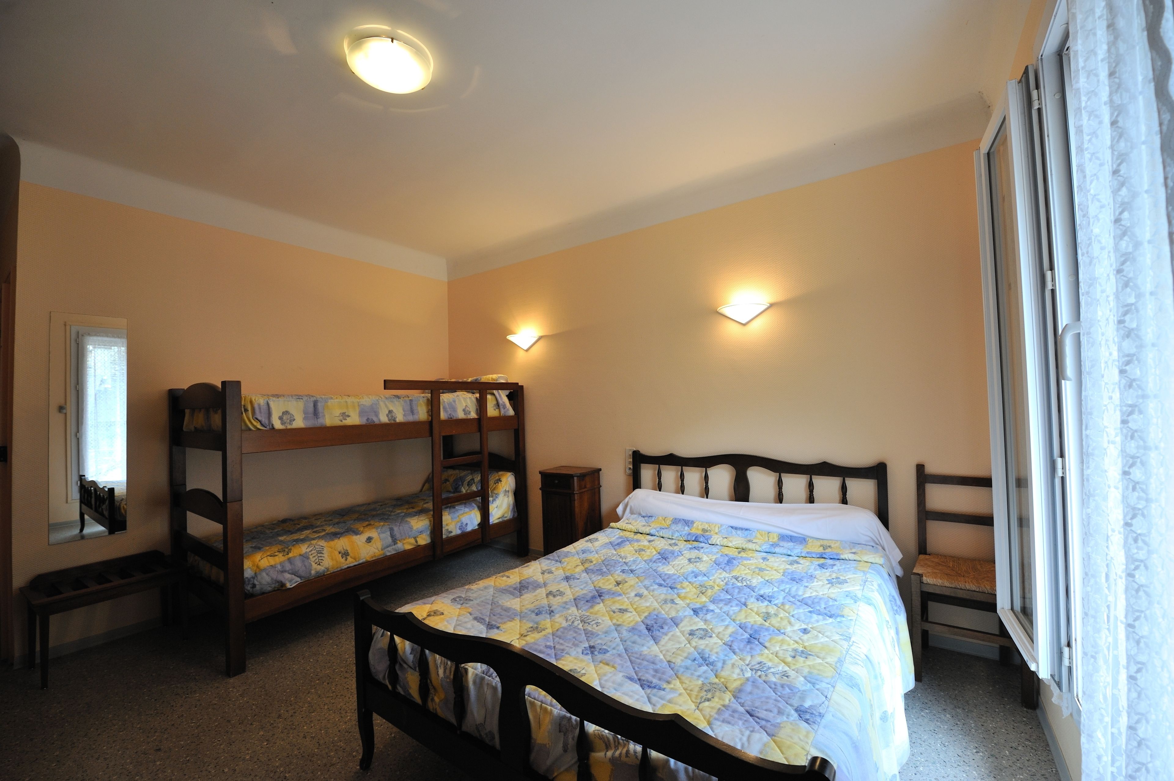 A bedroom with bunk beds, a single bed, a window with curtains, and wall-mounted lights.