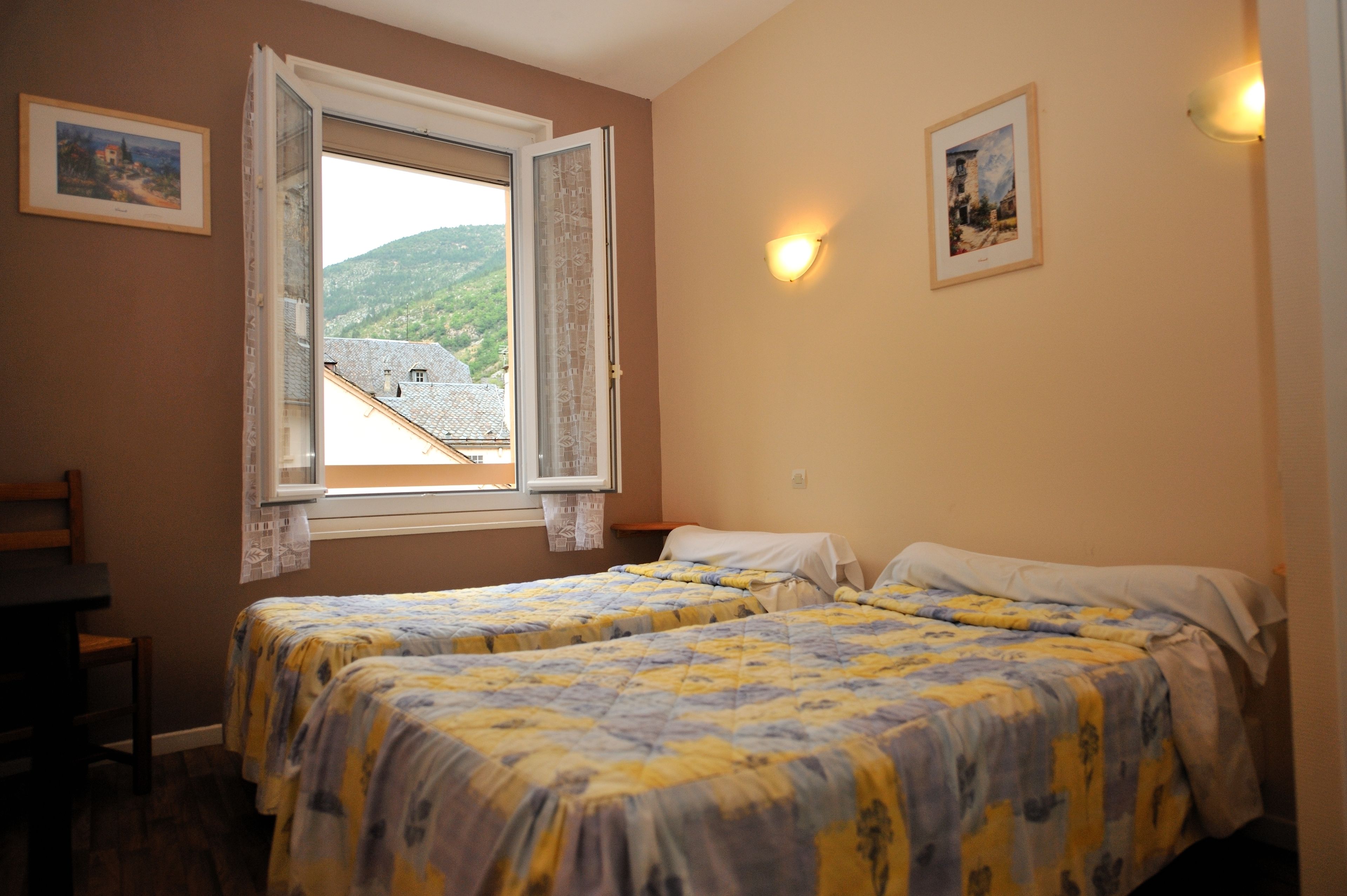 Une chambre avec deux lits, une fenêtre donnant sur une montagne et deux lampes fixées au mur.