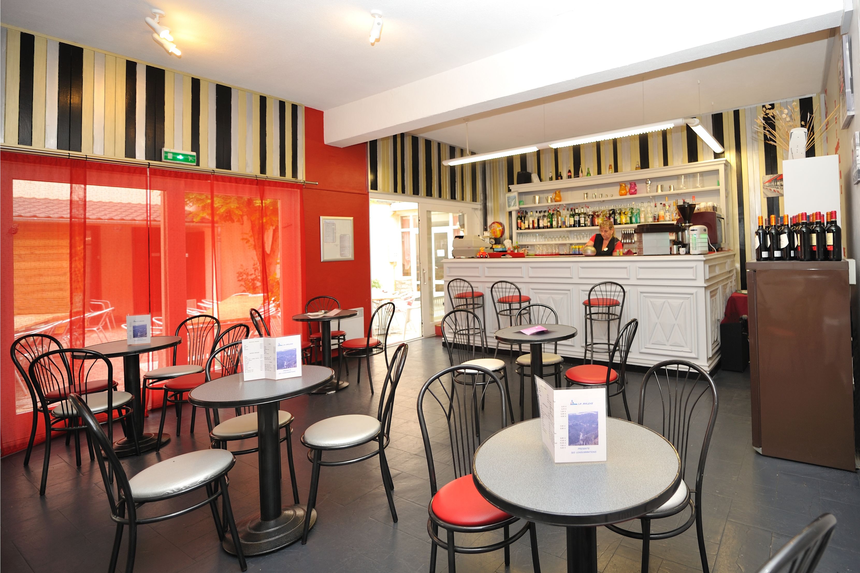 A restaurant interior with round tables, black chairs, and a bar area with shelves of bottles.