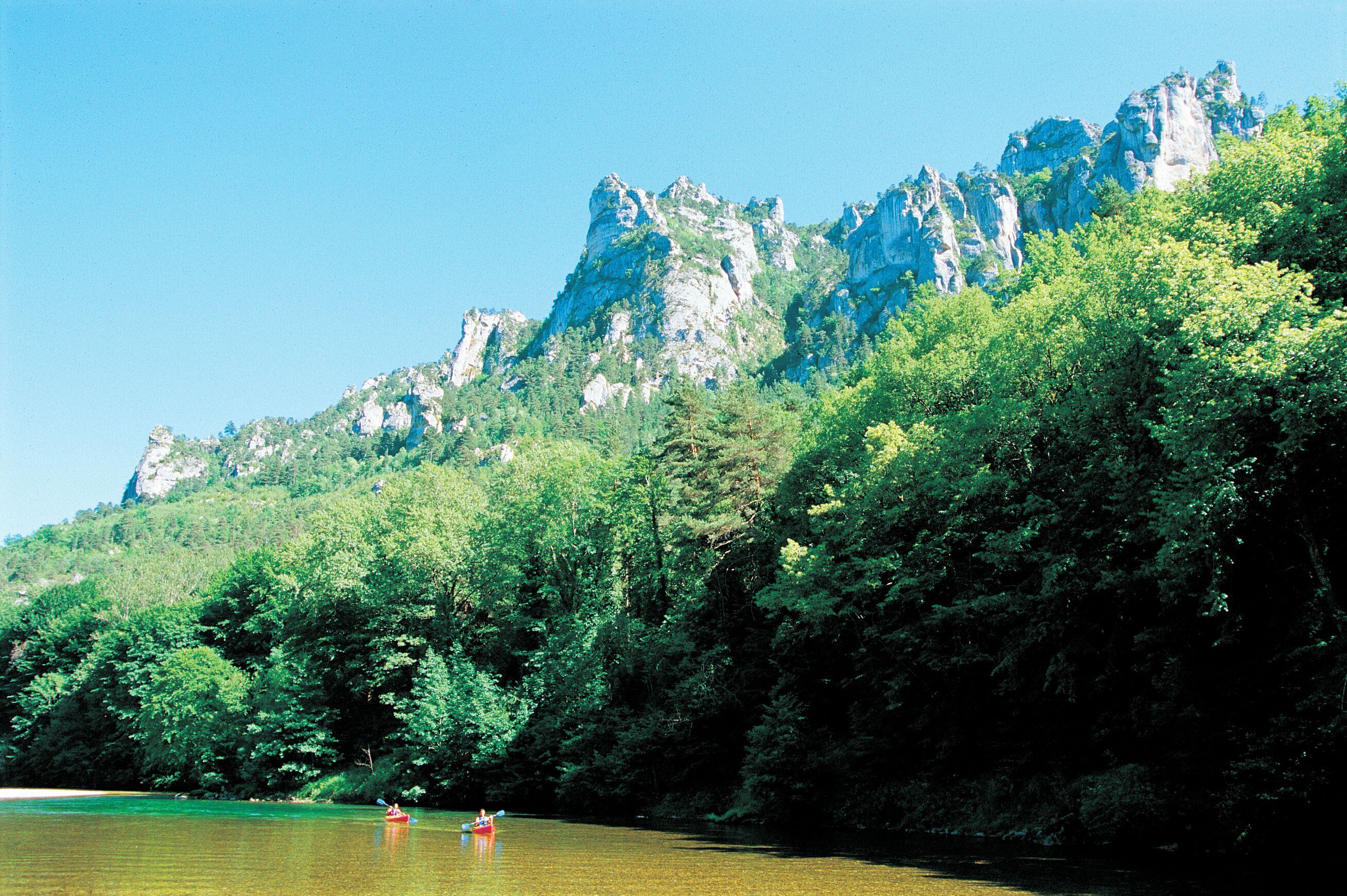 Un río con una montaña rocosa al fondo y abundante follaje verde a lo largo de la orilla.