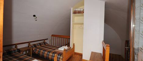 Una habitación pequeña y acogedora con dos camas de madera, una silla de madera y un armario blanco.