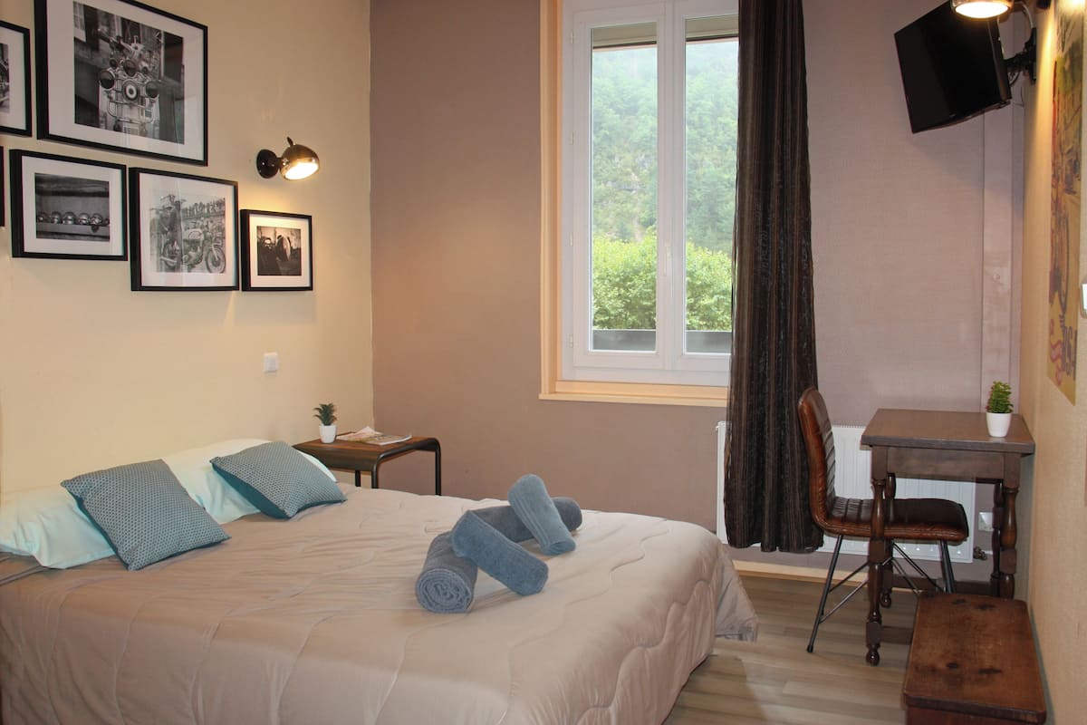 A bedroom with a bed, pillows, a desk, a chair, a TV, and framed pictures on the wall.