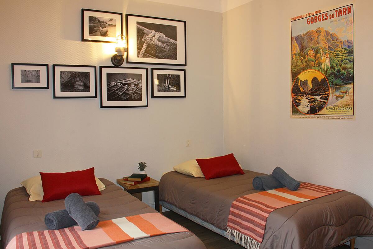 Ett hotellrum med två sängar, var och en med en röd kudde och en hoprullad handduk. Det finns inramade bilder på väggen och en affisch på väggen.