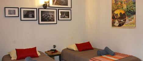 A hotel room with two beds, each with a red pillow and a rolled towel. There are framed pictures on the wall and a poster on the wall.
