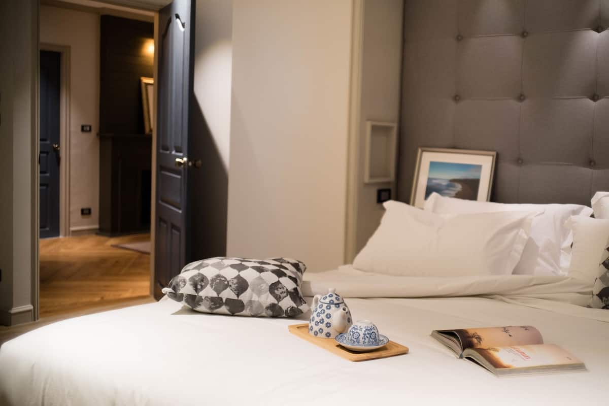 Ein Hotelzimmer mit einem Bett, Kissen, einem Tablett mit Teekanne und Tasse sowie einem Buch auf dem Bett.