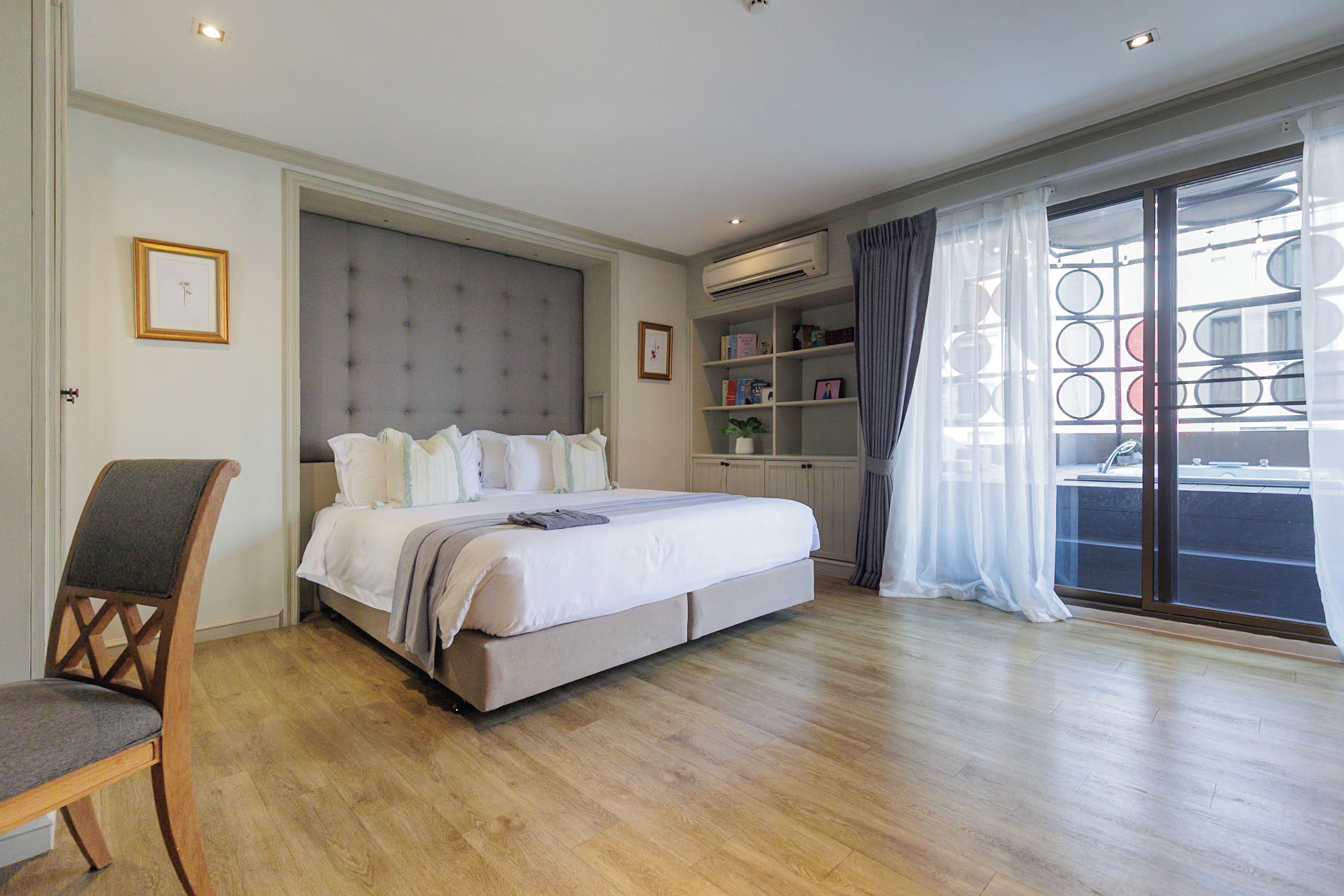 Een slaapkamer met een groot bed, een stoel, een boekenkast en uitzicht buiten door een raam.