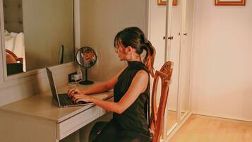 Uma pessoa sentada em uma mesa com um laptop, um espelho e uma pequena mesa com uma xícara.