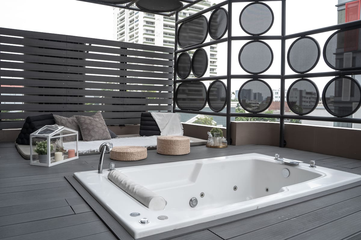 Ein moderner Außenbereich mit Spa-Einrichtung, inklusive eines großen, weißen Whirlpools, gepolsterten Sitzgelegenheiten und einer Wand mit runden Spiegeln.