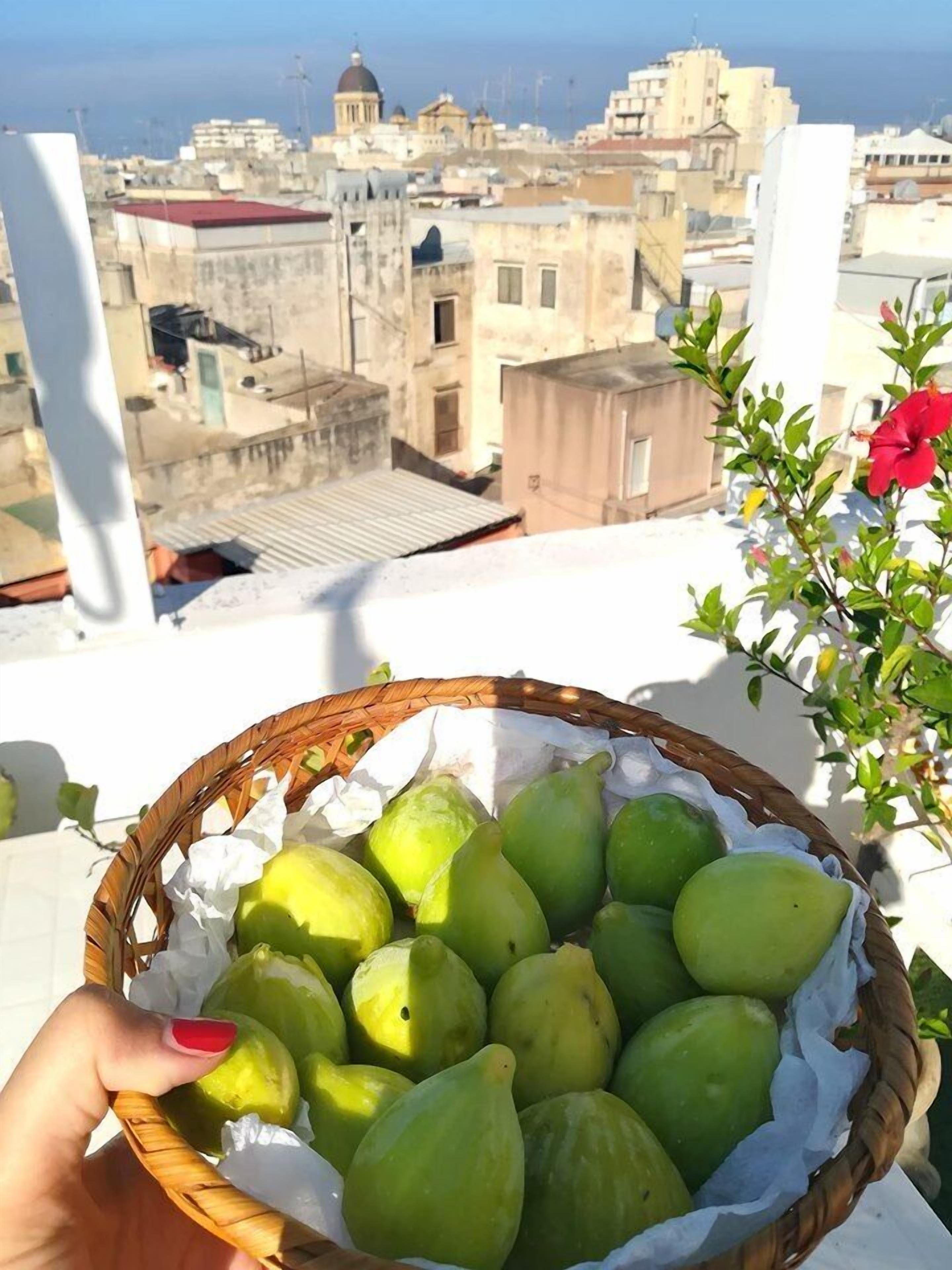 A hand holding a basket of green fruits on a balcony with a city view.