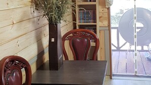 Un interior de madera con una mesa de comedor y sillas, una estantería y una ventana con cortina.