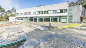 A modern building with large windows, a flat roof, and a paved courtyard with outdoor seating.