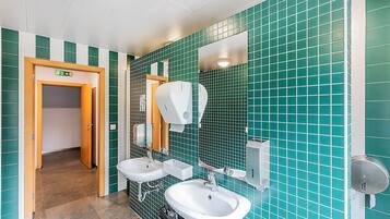 Un baño con paredes de azulejos verdes, dos lavamanos, un espejo y un secador de manos.