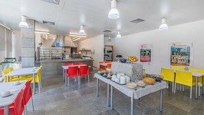 A modern dining area with tables and chairs, a kitchen in the background, and promotional posters on the walls.