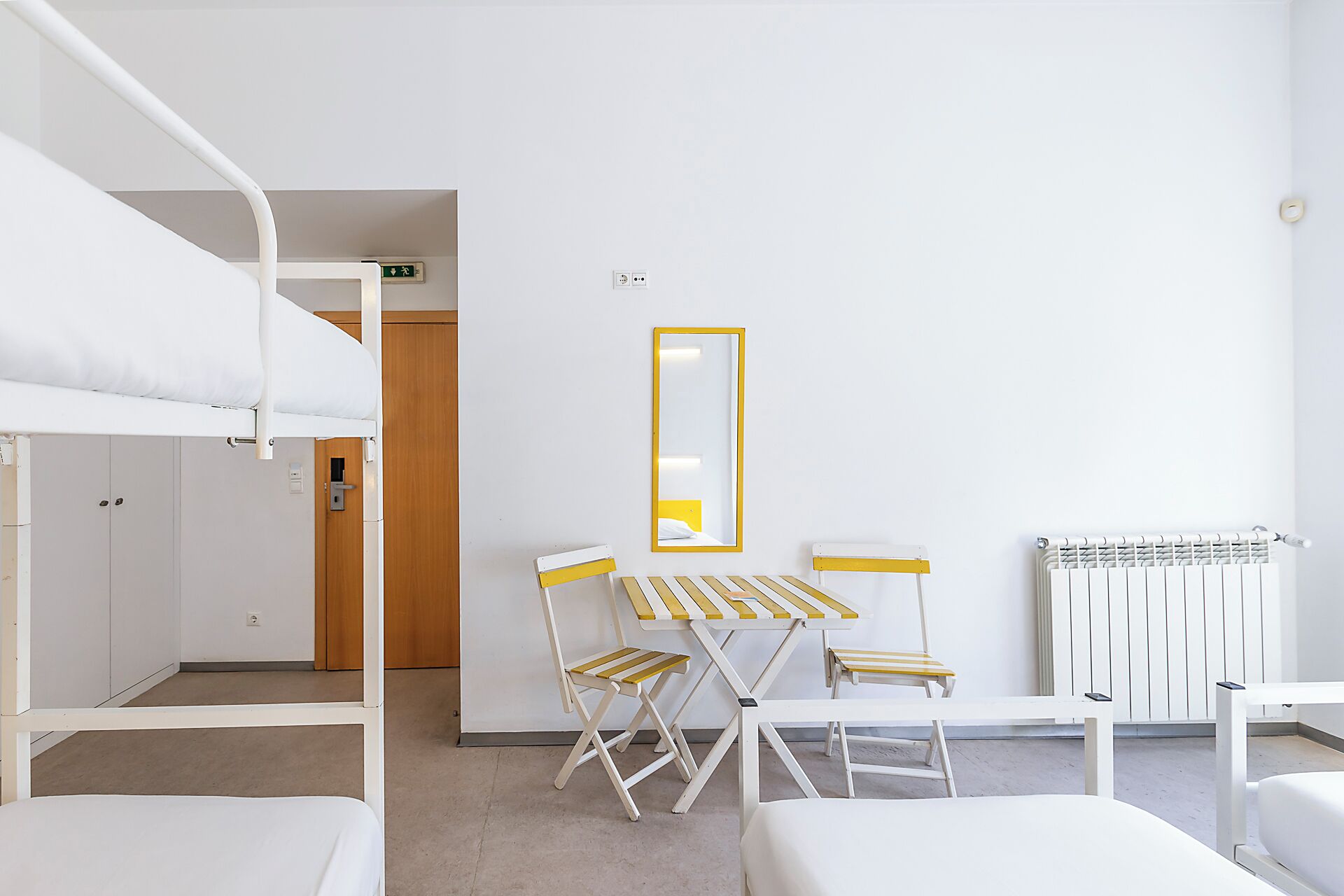 Una habitación de hotel con literas, una pequeña mesa con sillas, un espejo y un radiador.