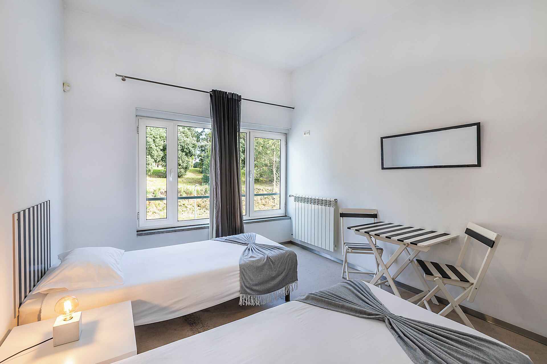 Une chambre avec deux lits, une fenêtre avec des rideaux, un radiateur, une chaise et une table.