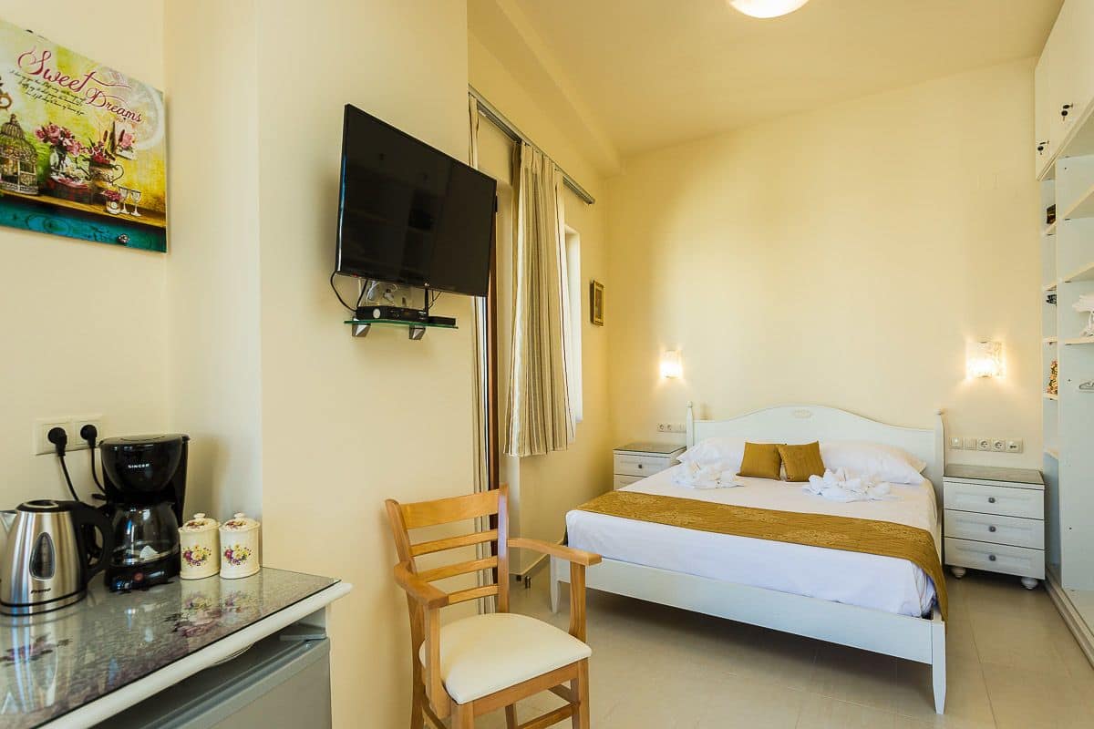 A hotel room with a bed, a TV mounted on the wall, a coffee maker, a chair, and a bedside table.