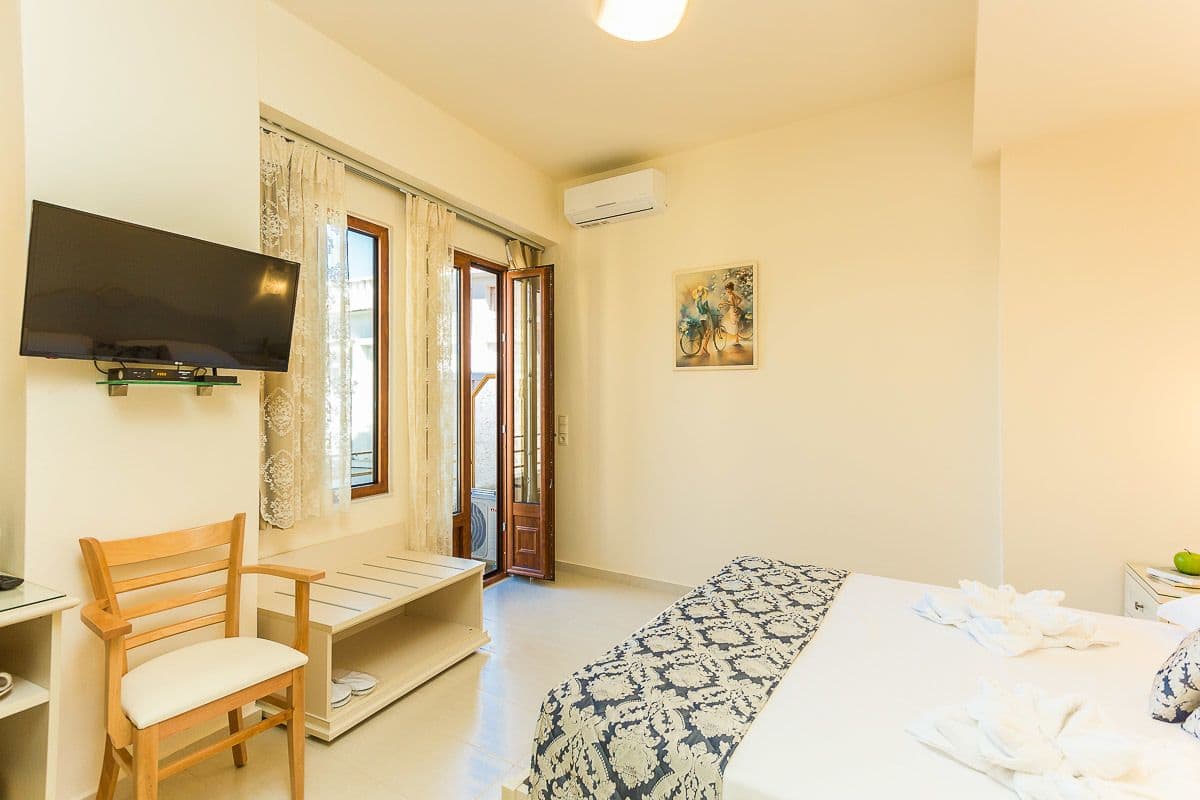 A bedroom with a bed, a TV mounted on the wall, a chair, and a window with curtains.