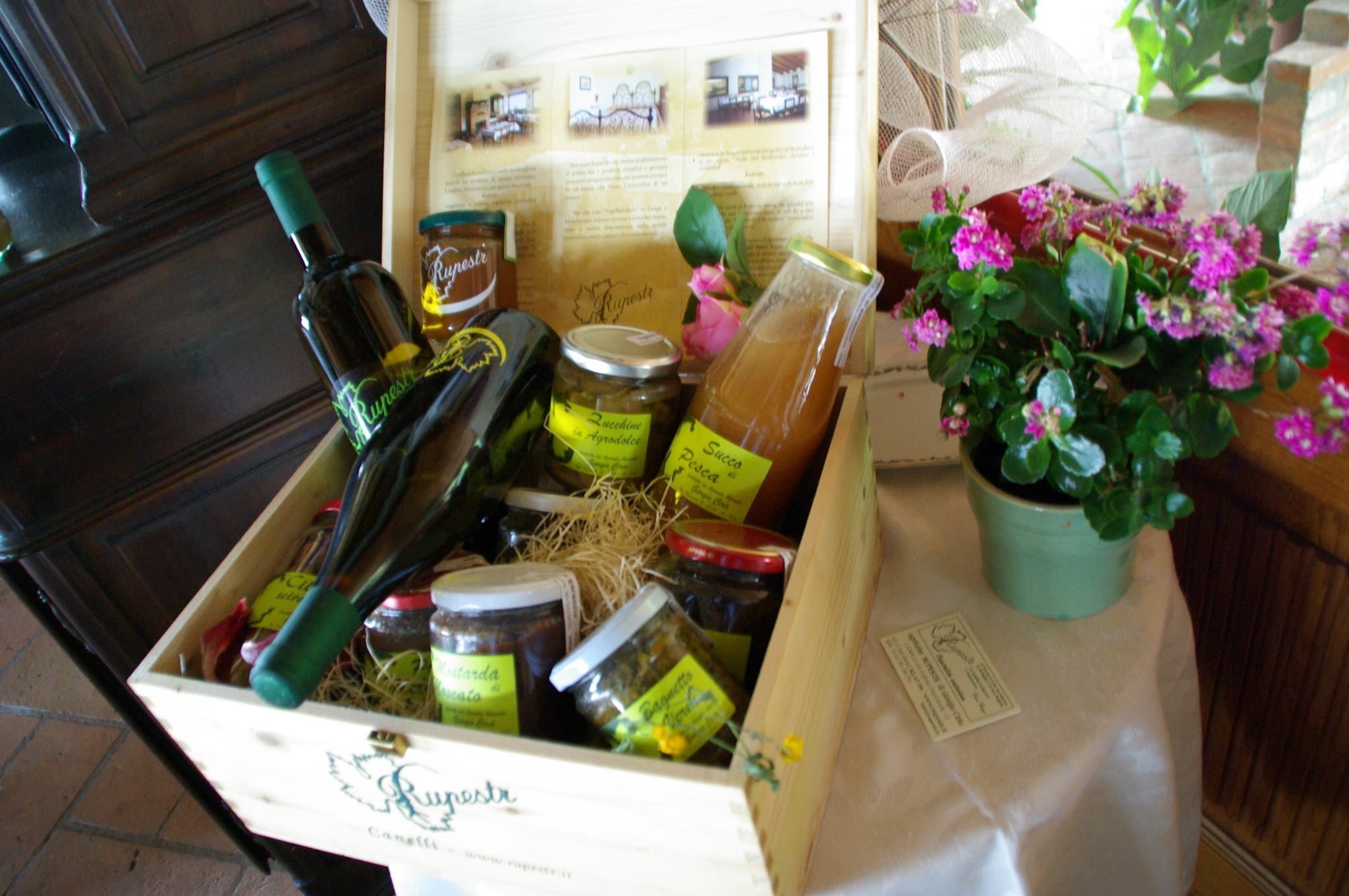 Una caja de madera llena de diversos alimentos y una planta en maceta con flores rosas.