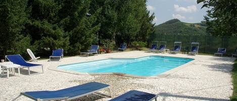 A pool area with lounge chairs and a clear blue pool surrounded by trees and a stone patio.