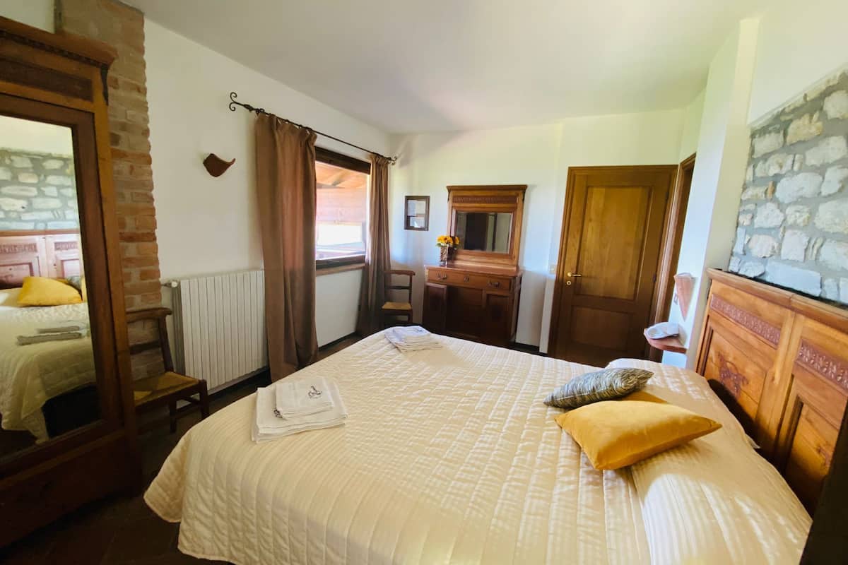 Une chambre à coucher avec un grand lit, une commode en bois, un miroir et une fenêtre avec des rideaux.