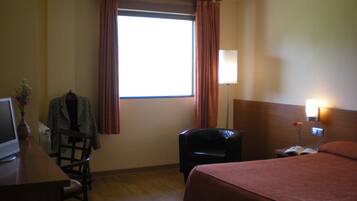 Una habitación de hotel con una cama, un escritorio con una computadora, una silla, una lámpara y una ventana con cortinas.